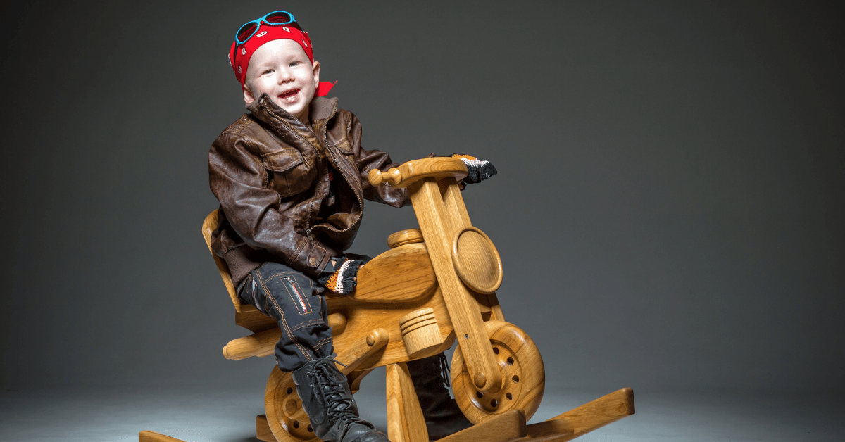 Kid sitting on a toy wood motorcycle