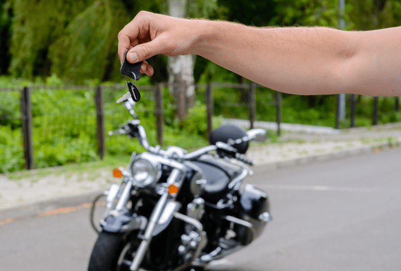 hand holding out motorcycle keys in front of a motorcycle