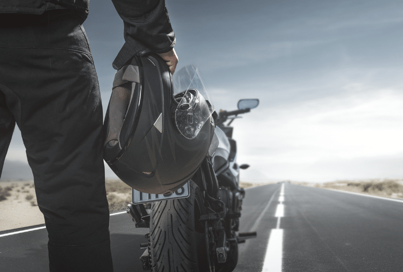 a man holding a motorcycle helmet standing in the road in front of his bike